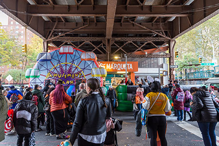 People in Halloween costumes walk under an elevated train in upper Manhattan